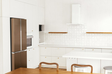 Modern kitchen interior. Stylish white kitchen cabinets with brass knobs, granite island and...