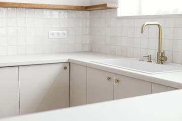 Modern kitchen interior. Stylish white kitchen cabinets with brass faucet, granite island, wooden shelves and appliances in new scandinavian house. Modern minimal kitchen design.