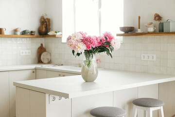 Beautiful peonies in vase on granite countertop island on background of stylish white kitchen with...