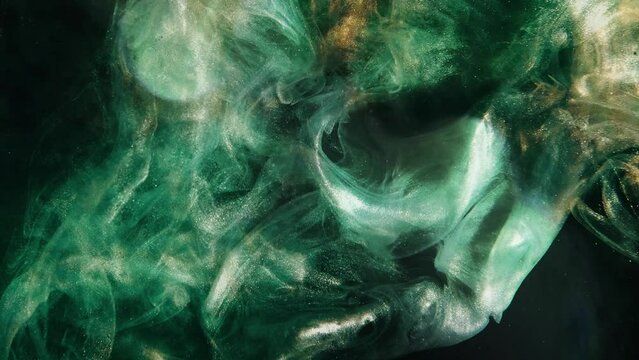 Ink water. Glitter fluid. Underwater splash. Abyss void. Green gold color glowing shiny dust particles smoke cloud floating on dark black abstract background.
