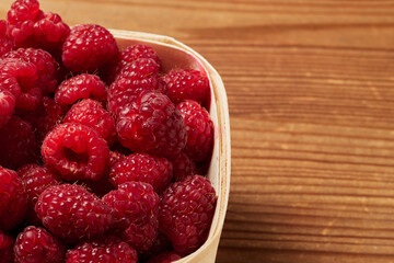 delicious fresh raw red raspberries in natural eco-friendly packaging in a basket of peeled hardwood veneer on a wooden table closeup. harvest. healthy food. diet. summer. vitamins