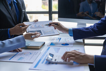 A group of young Asian businessmen brainstorm ideas looking at computers, laptops and financial documents. Collaboration and analysis of successful collaboration in office workspaces