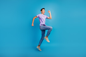 Fototapeta na wymiar Full length portrait of excited young man in t-shirt jumping success fast going over blue color background