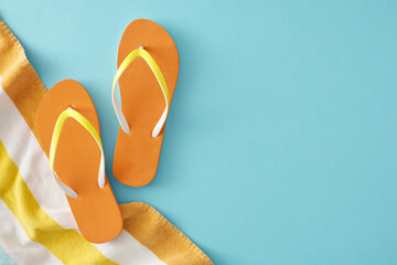 The idea of a summer beach relaxation period. Top view composition of striped towel, orange flip-flops on pastel blue background with empty space for ads or message