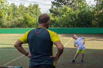 Warm-up before tennis practicing.6 years old boy repeats the stretching movements for his trainer