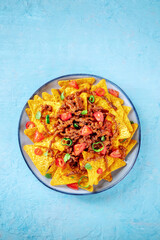 Nachos, Mexican food, tortilla chips with beef and fresh vegetables, overhead shot on a blue slate background