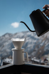 barista hand pouring filter coffee in cup with kettle outdoors in nature