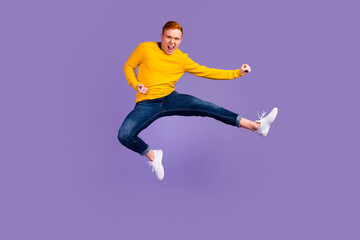 Fototapeta na wymiar Full length portrait of excited young man jumping while celebrating success isolated over violet color background