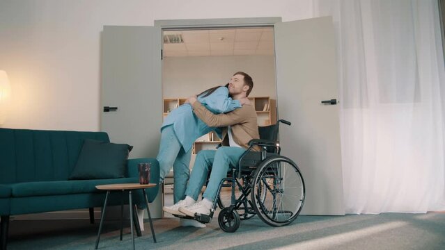 happy wife is giving an effective hug to her husband sitting in wheelchair as a sign of love and respect in room a sunny day