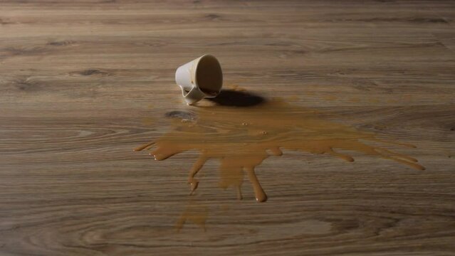 A cup of coffee with milk falls on the laminate and spills liquid on the floor.