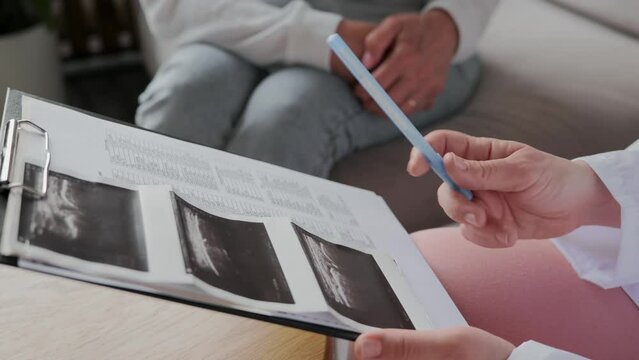 In close-up, the doctor examines the results of the ultrasound examination and explains the image to the patient by pointing to the defect with a pen. High quality 4k footage