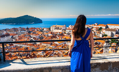 Fototapeta na wymiar Young Asian woman looking over the city of Dubrovnik on a clear summer day. Woman in blue summer dress. Europe Travel concept. Croatia Travel.