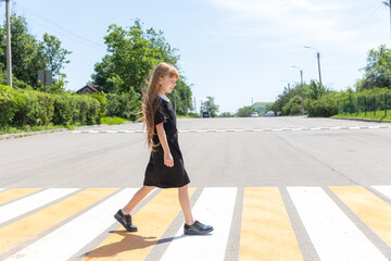 Schoolgirl crossing road on way to school. Zebra traffic walk way in the city. Concept pedestrians passing a crosswalk. Stylish little girl walking with backpack. Active child.