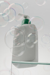 A white bottle with cosmetics on a glass shelf surrounded by flying bubbles. Shower gel, shampoo. 