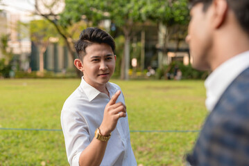 A cocky young asian man being a know-it-all and telling a colleague what to do while outside the office.