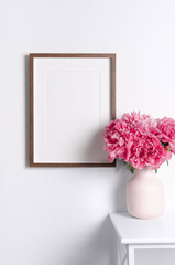Vertical picture frame mockup on white wall with pink peony flowers bouquet