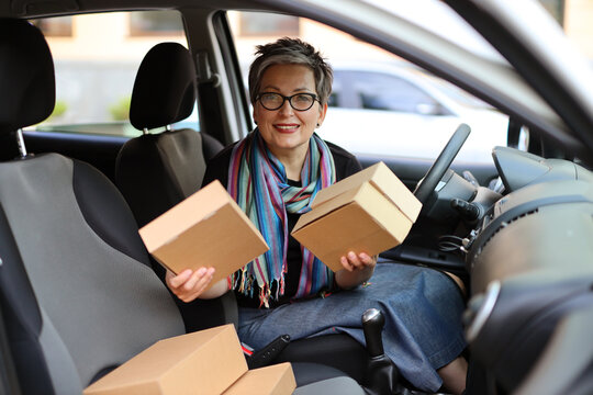 Happy woman in a car with parcels in her hands. The concept of online shopping and sending or receiving orders.