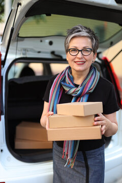 Beautiful adult woman with parcels in her hands with a car with an open trunk in the background.