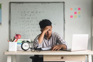 Frustrated tired high school teacher sitting on desk in classroom