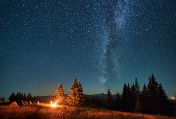 Night camping in mountains under starry sky. Tourist tents in campsite under sky full of stars with...