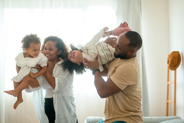 Naklejka premium Happy African American Parents with little daughters playing on the bed in bedroom at home, happy family concept