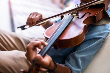 Selective focus to the violin with an old musician is playing it. Street musician in Bangkok.