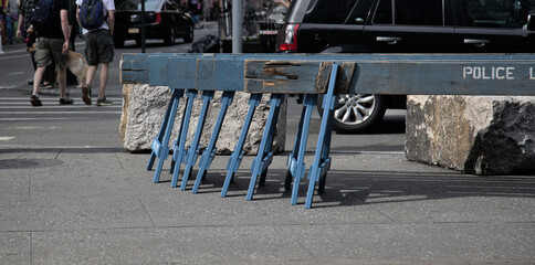 police barricades stacked on a sidewalk next to an intersection crosswalk (car and people passing)...