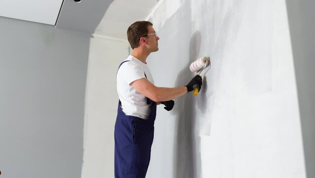 Young painter holds paint roller and painting a wall. Painting interior wall with paint roller in new house. Home decoration concept