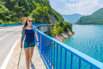 Young woman walking on the bridge across Piva lake in Montenegro. Female tourist spending time on vacations near the lake