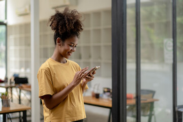 Young African American woman standing in modern office, freelance business using mobile phone.