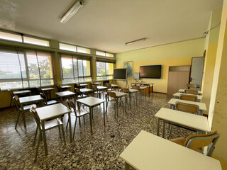 school classroom with empty chairs and desks without students with a geographical map, monitor and blackboard