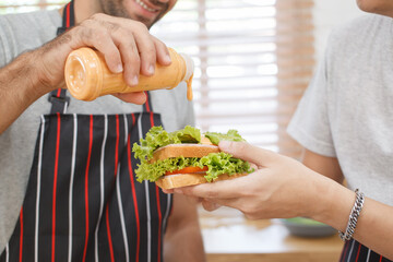 Happy cheerful LGBTQ+ gay romantic couple preparing and making their breakfast together in the kitchen. Diversity in ethnicity, nationality, and sex concept. LGBTQ+ married people lifestyles.
