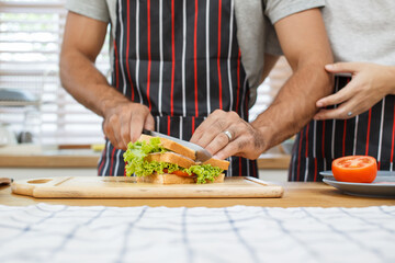 Happy cheerful LGBTQ+ gay romantic couple preparing and making their breakfast together in the kitchen. Diversity in ethnicity, nationality, and sex concept. LGBTQ+ married people lifestyles.
