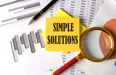SIMPLE SOLUTION text on a sticky on the graph background with pen and magnifier