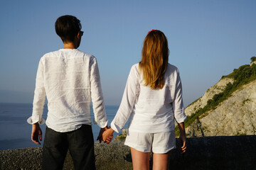 young couple in white summer clothes hold hands and enjoy the view of the sea amalfi coast