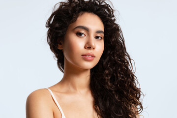 A girl with glowing skin and thick black and curly hair looks at the camera against a blue background