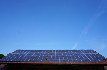 Großes Dach mit blauen Solarpanels von Haus vor blauem Himmel bei Sonne am Mittag im Sommer