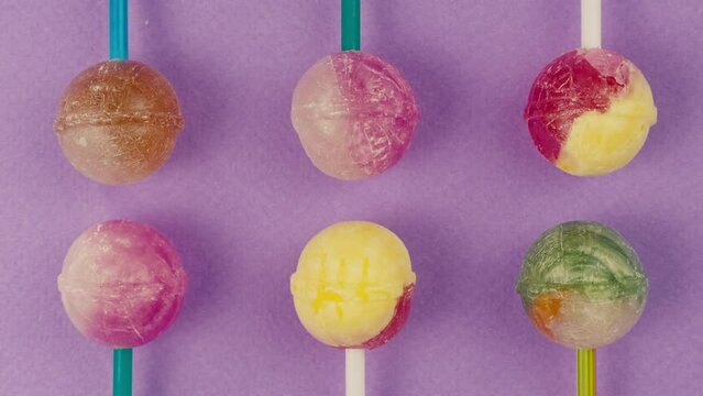 Sweet lollipops with glitter sprinkles on color purple background. Bright texture sugar candies close up top view. Composition of favorite children's summer sweets. Studio shot for shop, supermarket