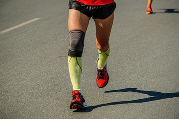 close-up legs male runner in compression socks and knee pads running marathon race, sports summer...