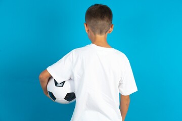 Little hispanic boy wearing white T-shirt holding a football ball hugging herself happy and positive from backwards. Self love and self care