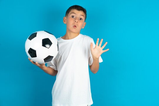 Little hispanic boy wearing white T-shirt holding a football ball Moving away hands palms showing refusal and denial with afraid and disgusting expression. Stop and forbidden. - Powered by Adobe