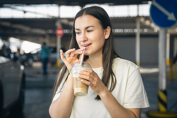 A young woman drinking coffee in the parking lot.