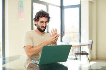 young adult bearded man with a laptop feeling anxious, sick and unhappy, suffering a painful hand ache