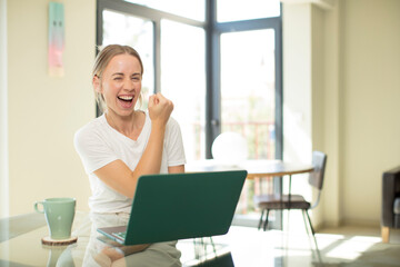 caucasian pretty woman with a laptop feeling happy, satisfied and powerful, flexing fit and muscular biceps, looking strong after the gym