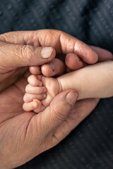 The handle of a newborn in the hands of a grandmother, close-up.