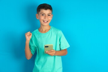 Portrait of Little hispanic boy wearing green T-shirt holding in hands cell celebrating