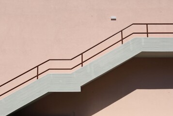 Concrete staircase with brown metallic railing on pink painted facade. Background for copy space.