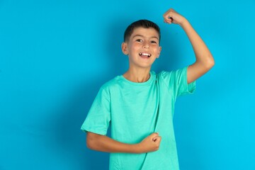 Profile photo of excited Little hispanic boy wearing green T-shirt good mood raise fists screaming...
