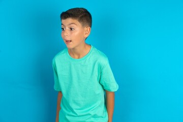 Little hispanic boy wearing green T-shirt stares aside with wondered expression has speechless...