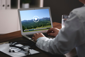 Doctor watching video on laptop at office desk, closeup. Man choosing vacation spots